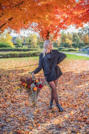 A fashionable autumn portrait with a woman posing with flowers under bright orange foliage.
