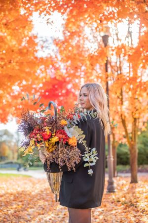 A woman holding a seasonal floral arrangement against a backdrop of brilliant fall colors.