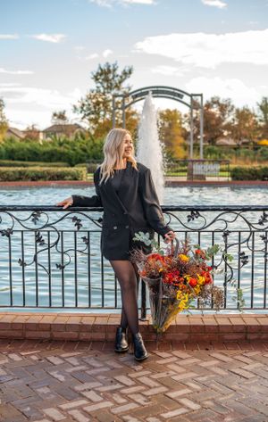 A stylish portrait by a fountain featuring fall flowers and an ornate iron railing.