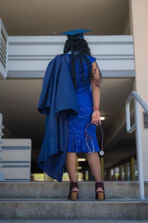 Graduate in royal blue dress and cap standing on stairs with flowing cape.