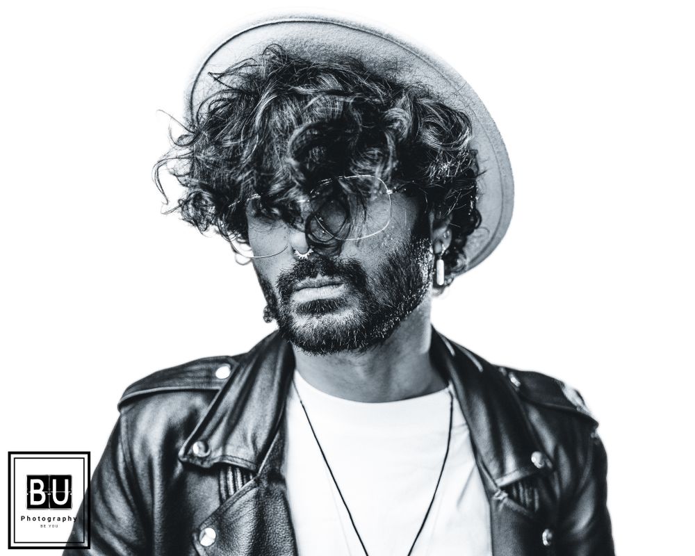Black and white portrait of person in leather jacket and hat with curly hair.

- BU Photography -