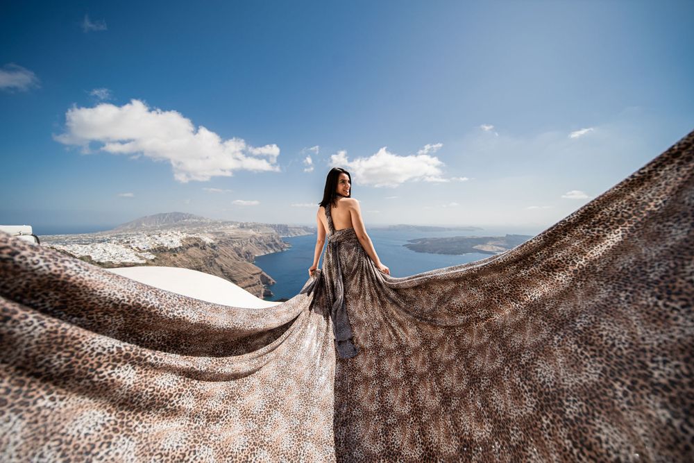 Brown flowing dress catches wind against stunning Greek island vista and blue sea.