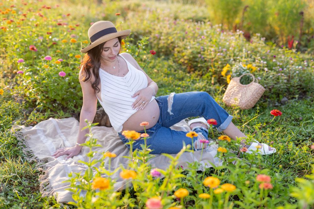 Maternity portrait in garden with woman relaxing among yellow and pink flowers.