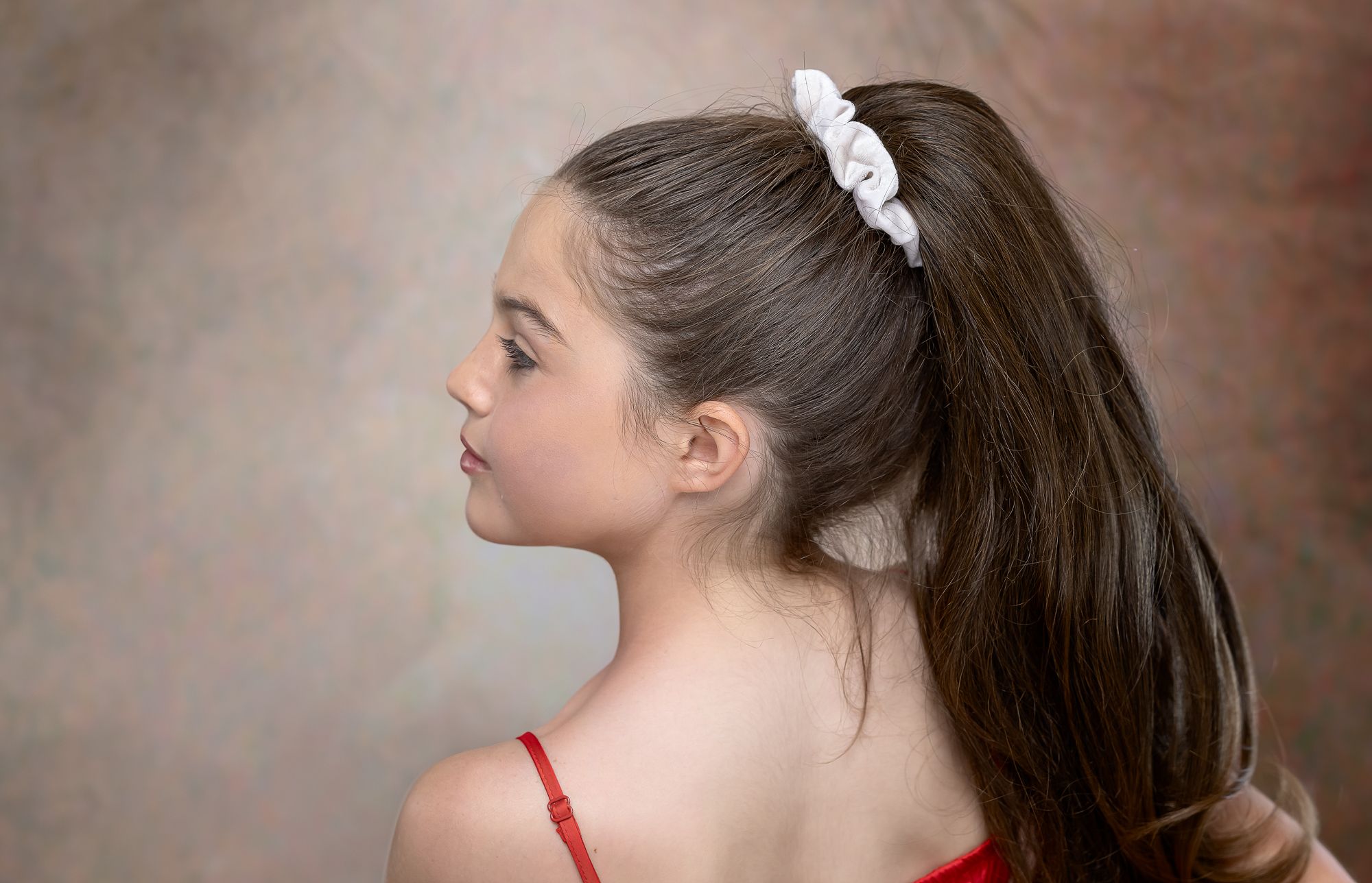 Artistic profile portrait showing ponytail and bare shoulders against muted brown background.