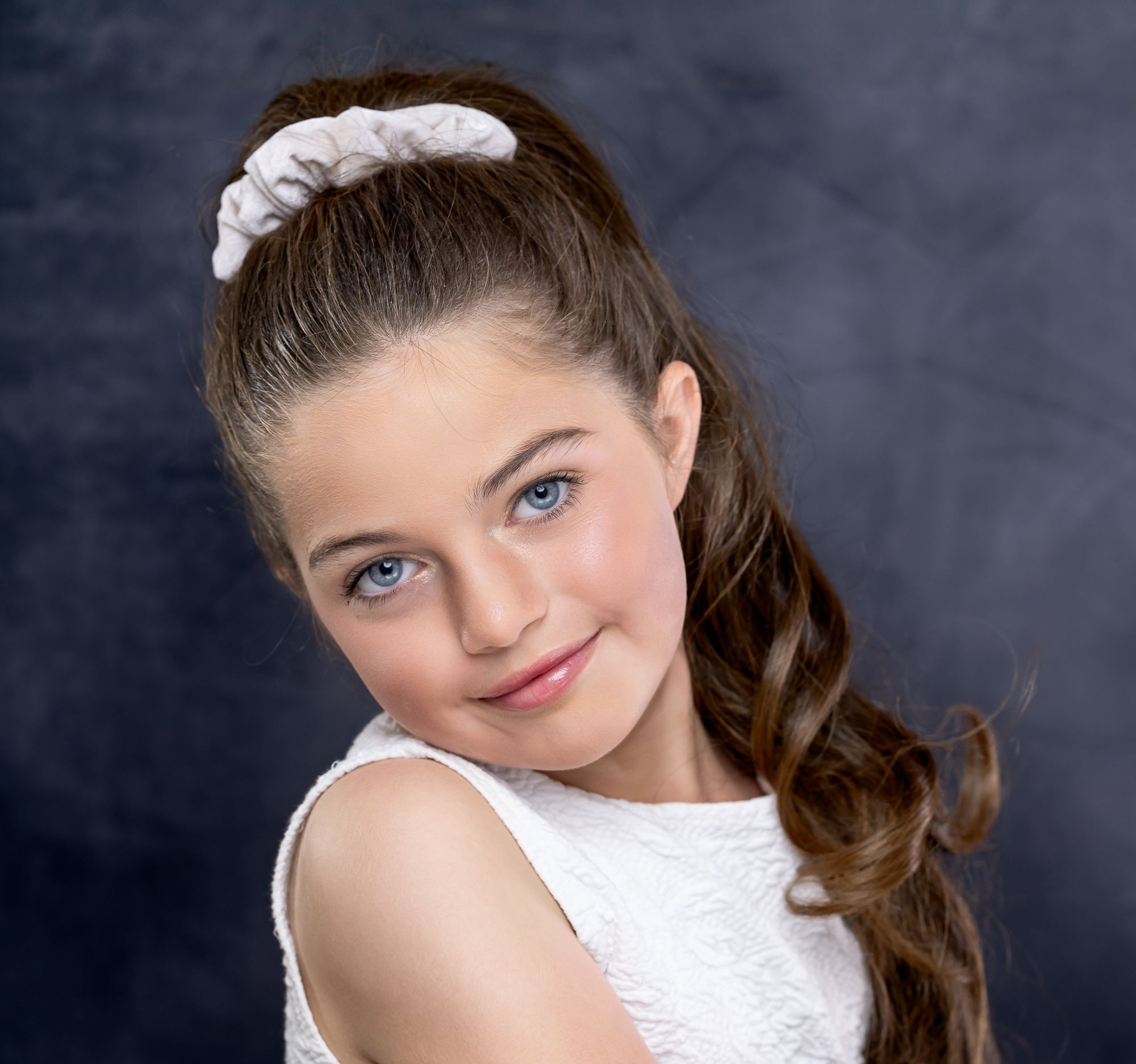 Studio portrait of a young person in white dress with curled brown hair and floral headband.