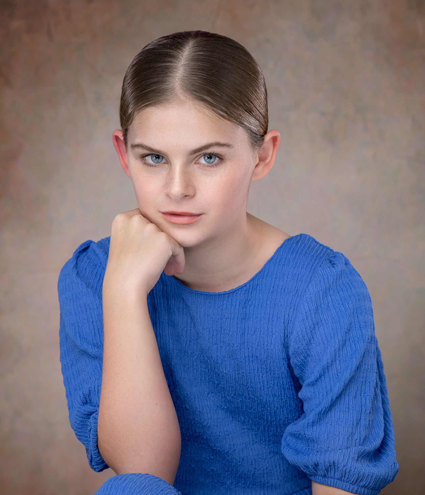 Portrait of person in royal blue blouse with thoughtful expression against neutral backdrop.