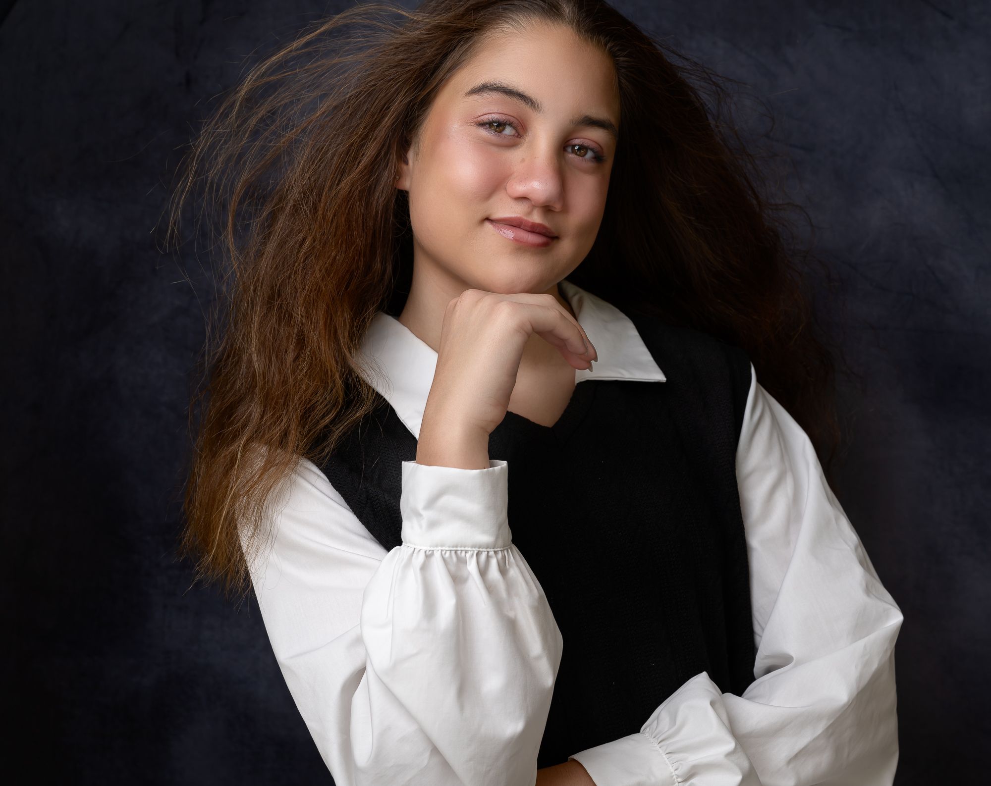 Portrait in vintage-style outfit with white shirt and black vest against textured dark background.