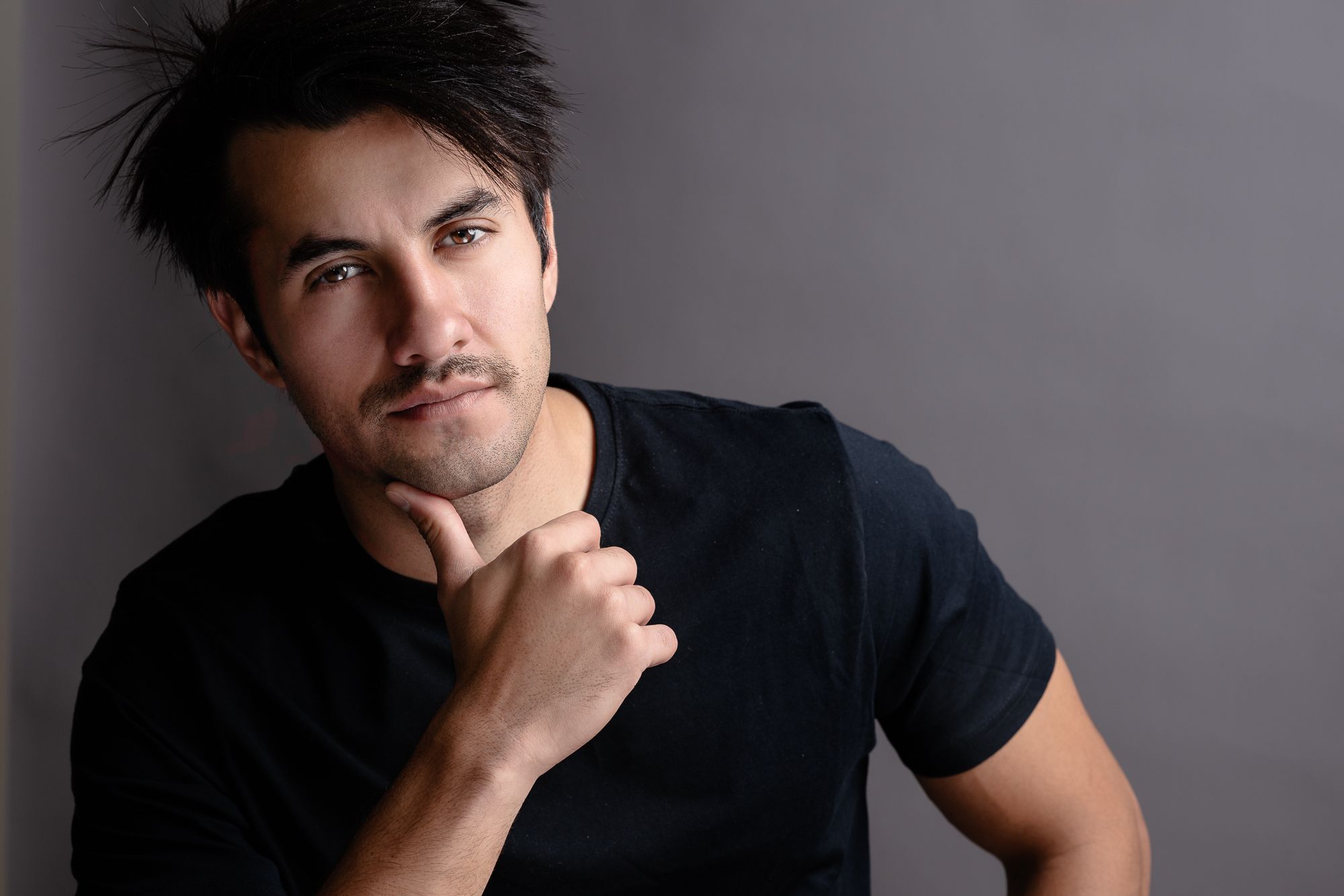 A dramatic studio portrait of a person in a black t-shirt against a gray background.