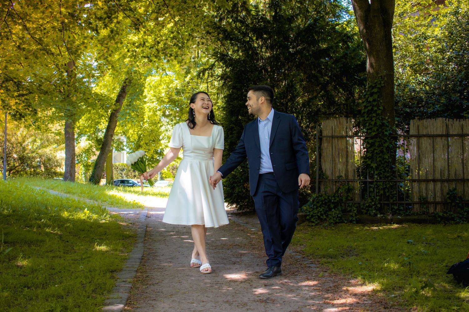 Couple walking along tree-lined path in summer garden setting.