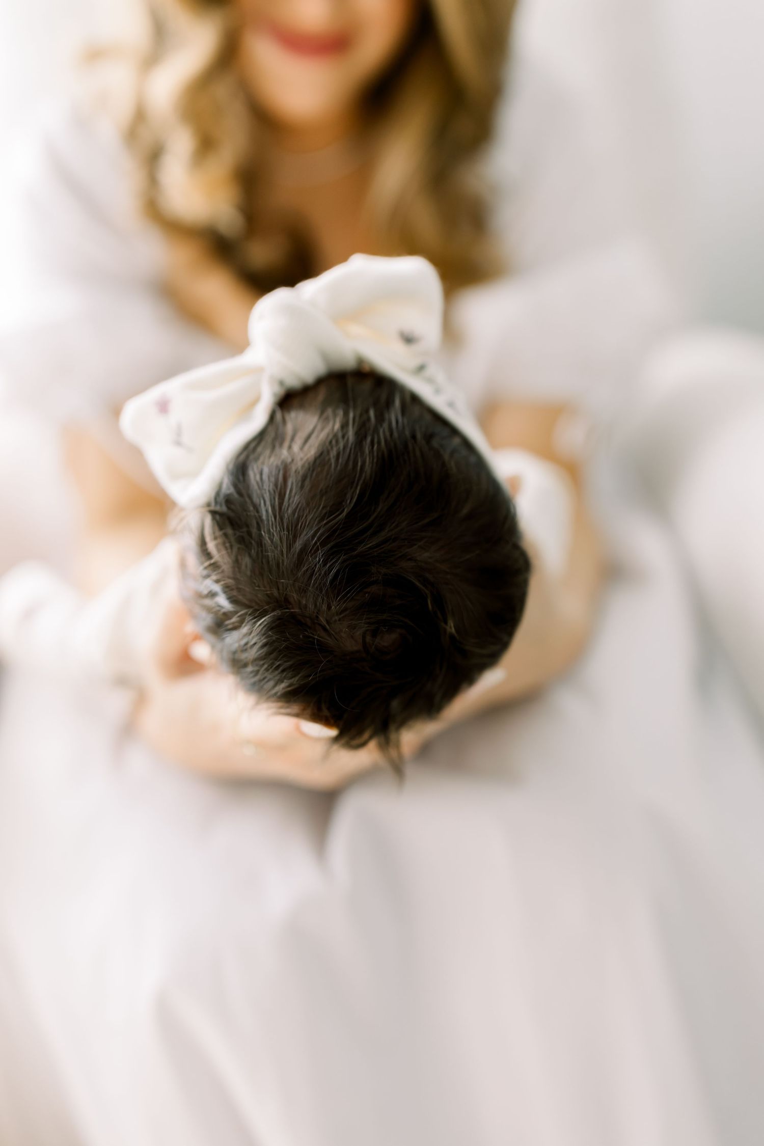 Overhead view of a baby wearing a white bow while resting on soft bedding.