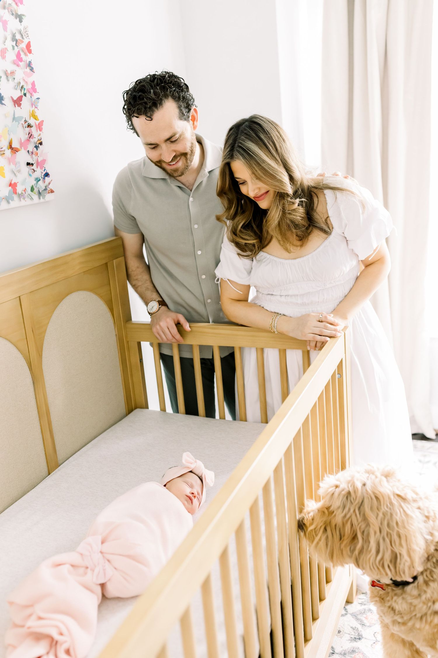 Couple looking lovingly at baby in wooden crib with dog nearby.