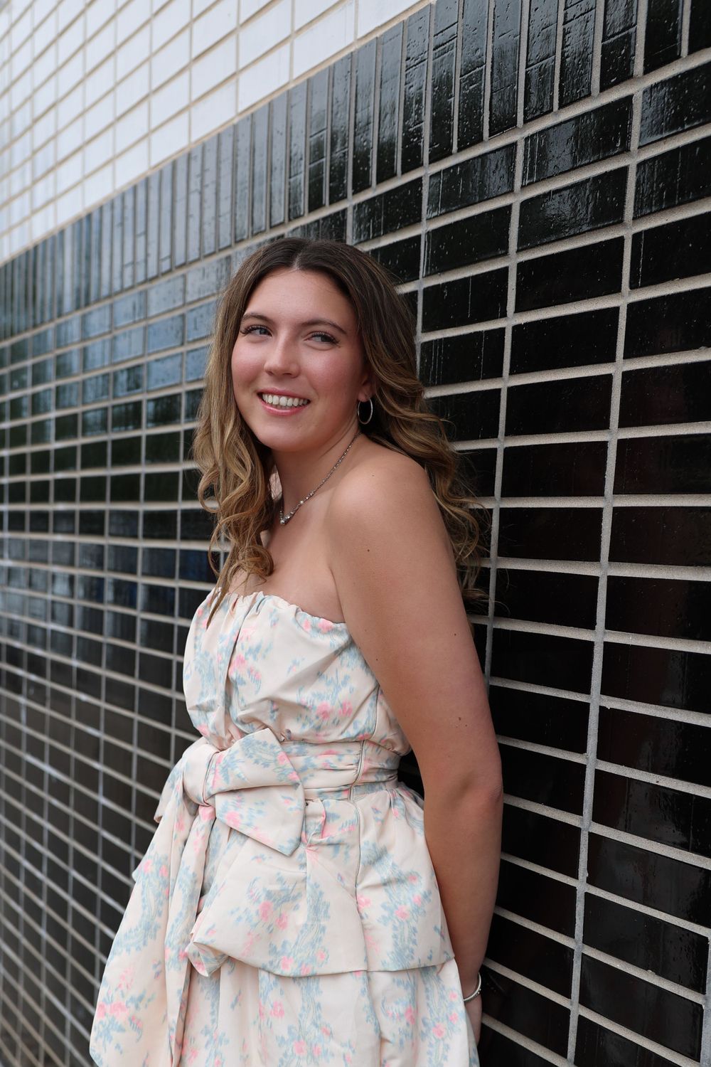 Summer fashion portrait showing a floral strapless dress against a modern tiled wall backdrop.