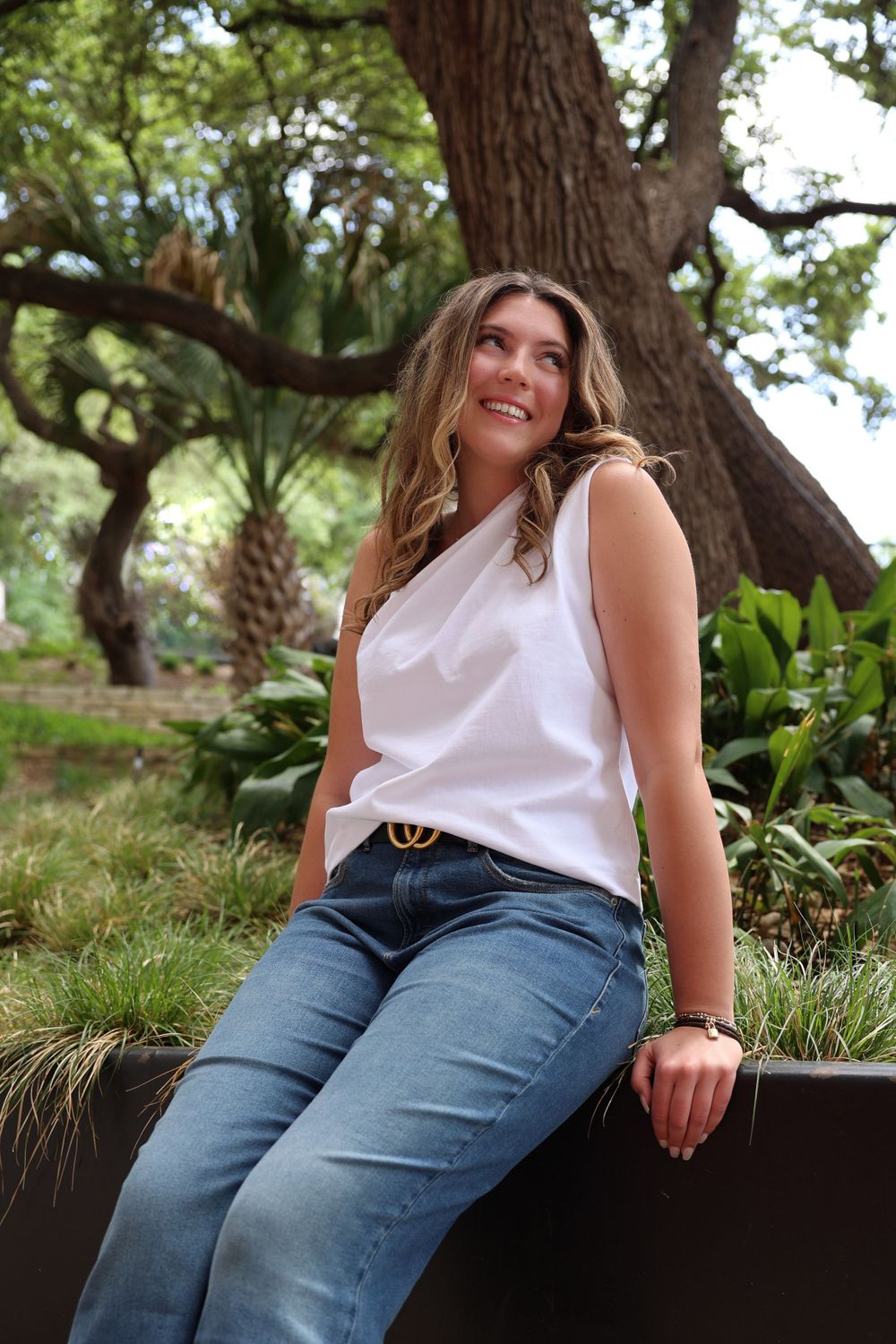 Outdoor portrait with white sleeveless top and jeans beneath large oak tree in garden setting.