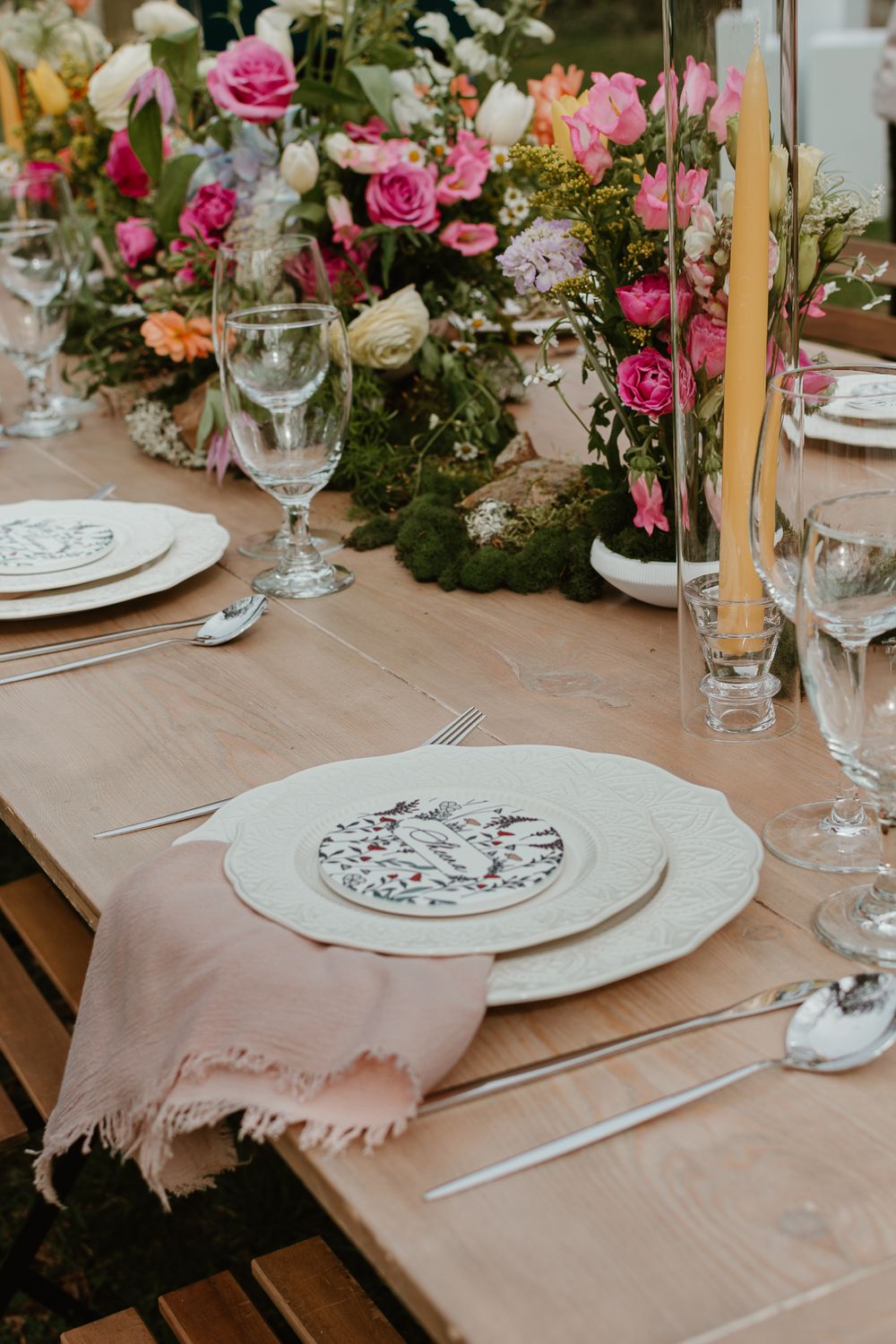 Pink and white floral centerpieces adorn an elegant table setting with scalloped plates.