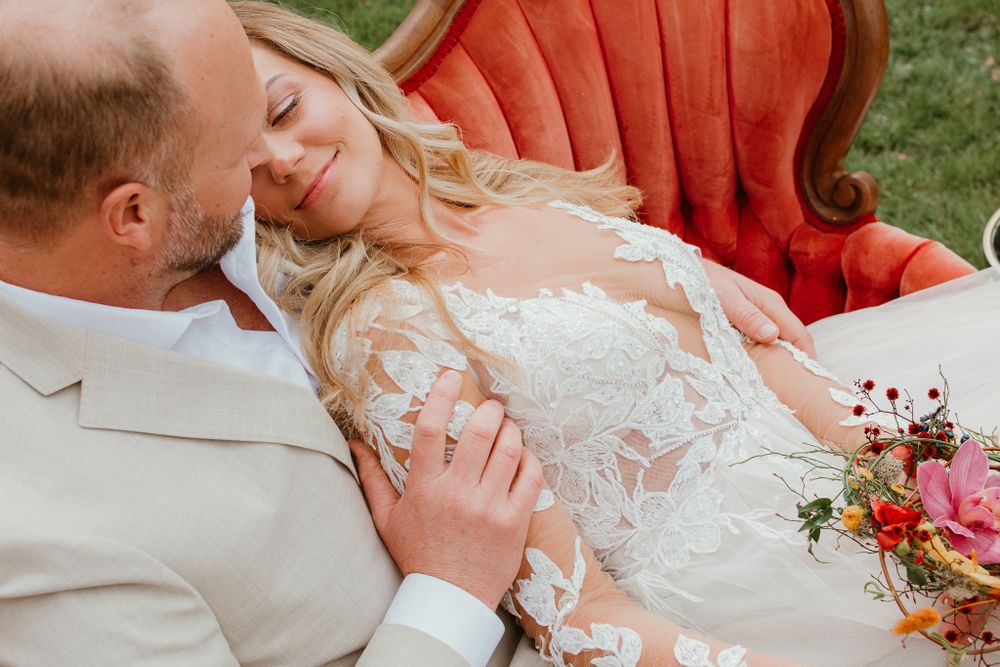 Romantic wedding portraits on orange velvet seating with floral bouquet.