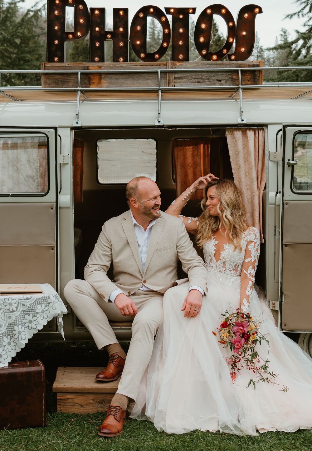 Wedding couple posing by vintage VW bus with string lights and rustic decor.