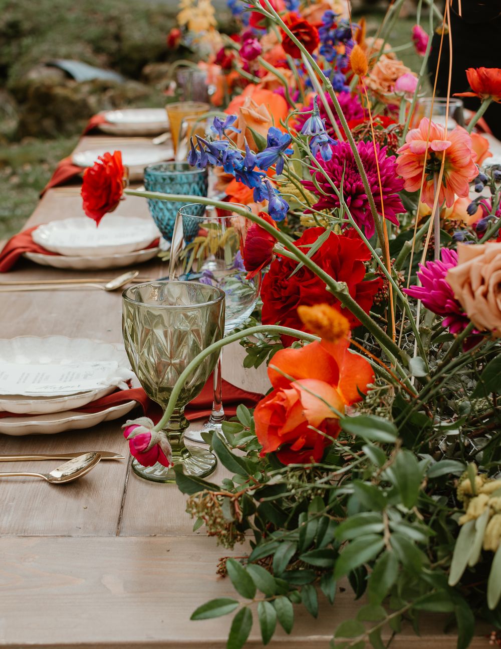 Vibrant red and orange floral arrangements line a rustic wooden dining table.