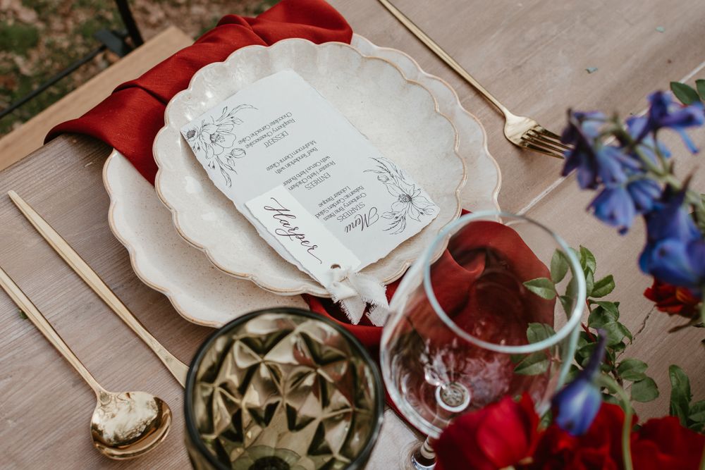 Elegant place settings with red flowers and delicate menu cards on wooden surface.