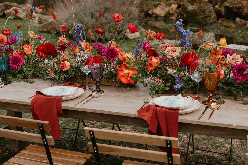 Outdoor dining setup with vibrant red and orange floral arrangements on wooden tables.