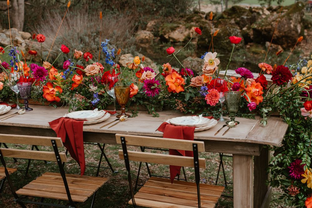 Long wooden tables decorated with colorful floral arrangements and place settings for outdoor dining.