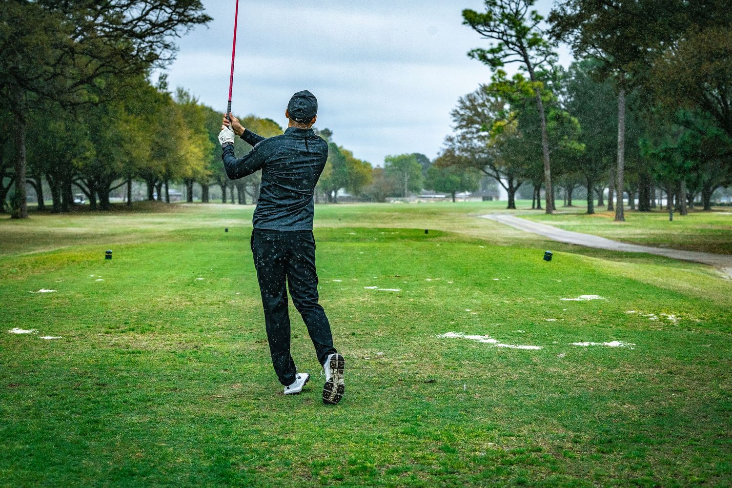 Golfer in dark attire follows through on their swing on a lush green course.