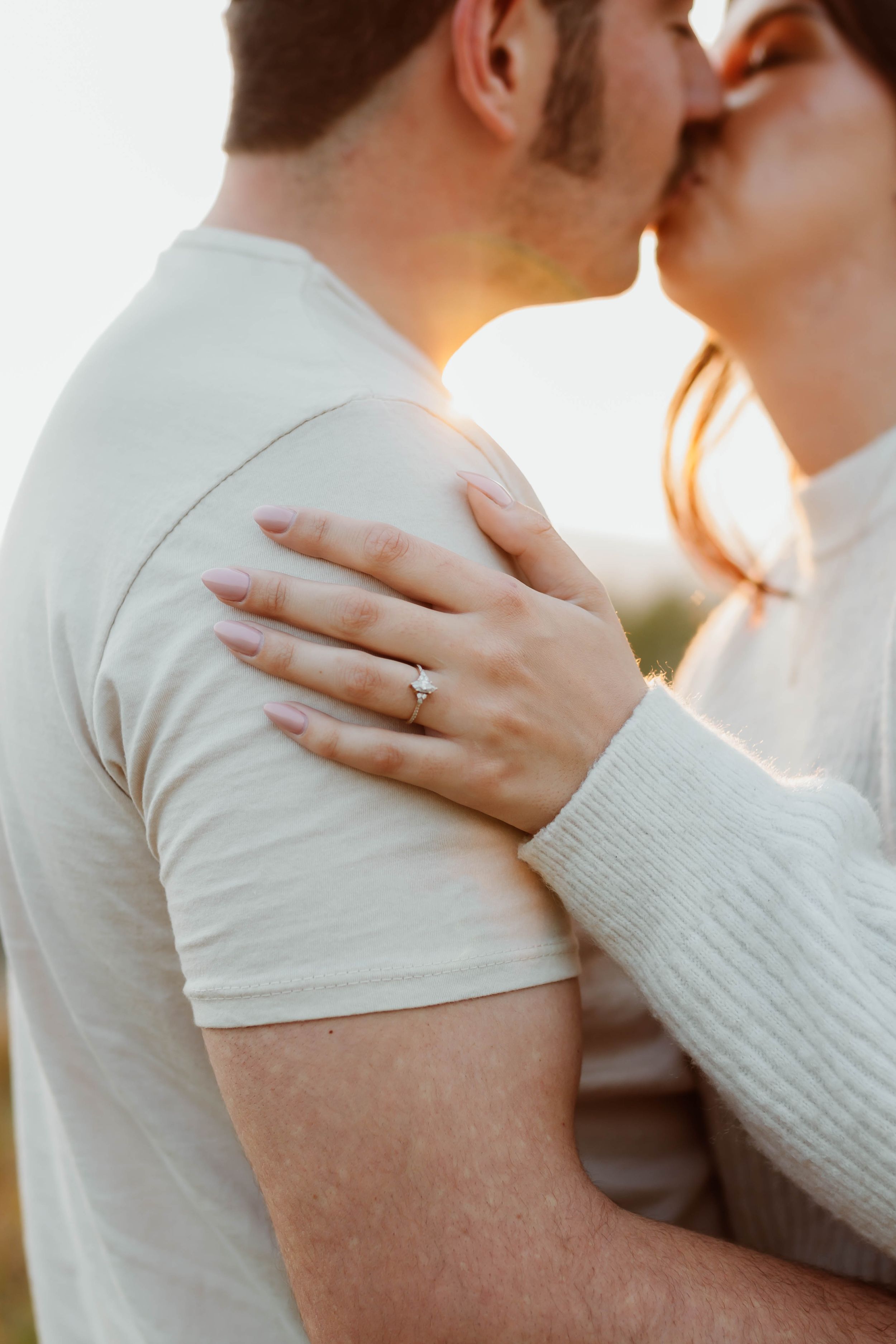 Close up shot of couple embracing with an engagement ring visible during golden hour.