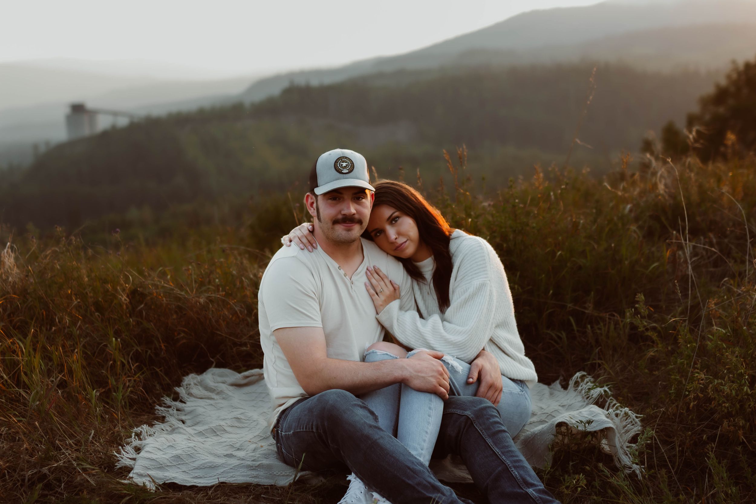 Couple sits together on mountainside during sunset engagement photo session.