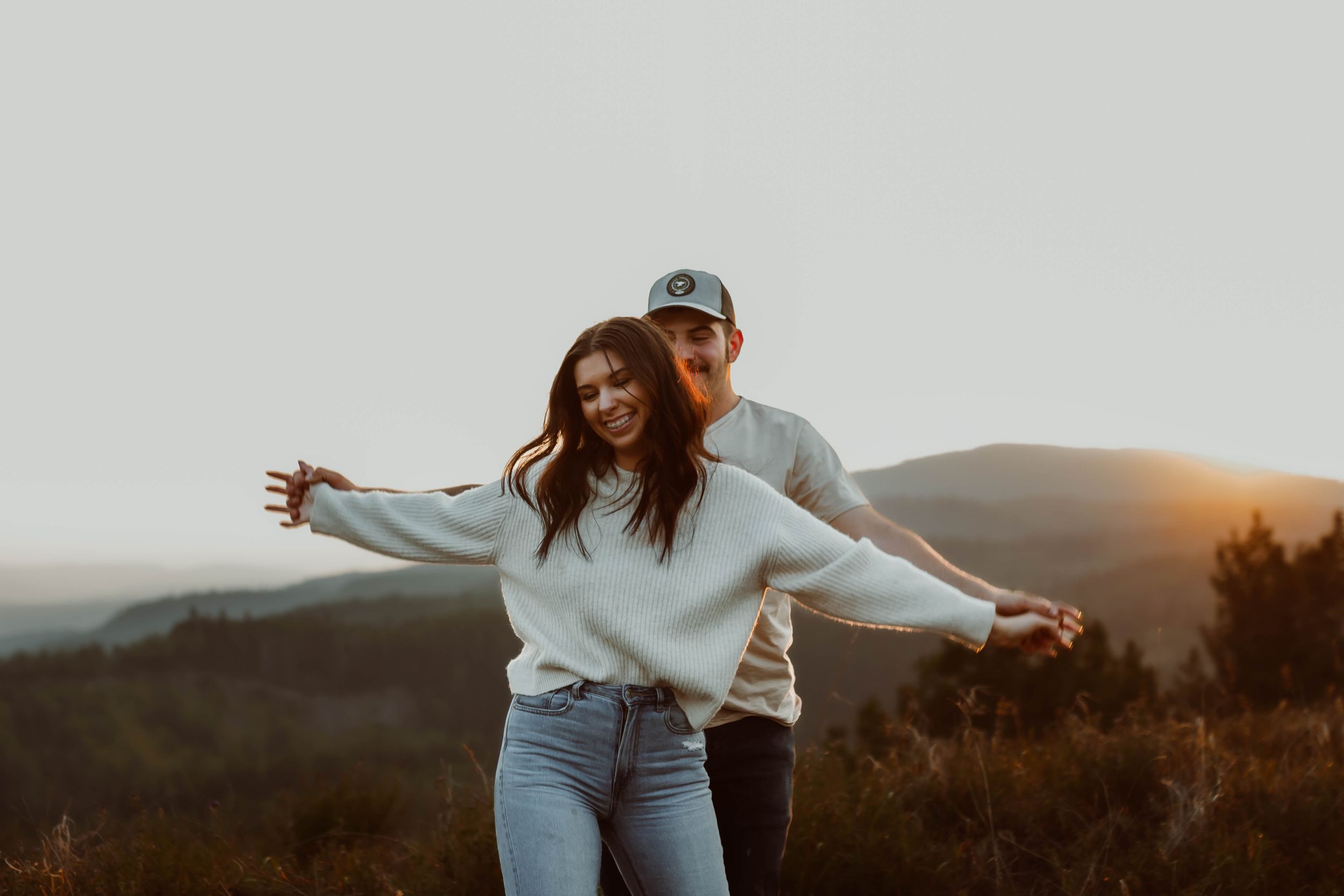 Playful couple poses together against mountain backdrop during sunset engagement shoot.