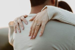Close-up shot of hands embracing with an engagement ring visible in soft lighting.