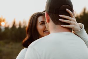 Romantic couple embracing outdoors during golden hour with woman smiling behind man's shoulder.