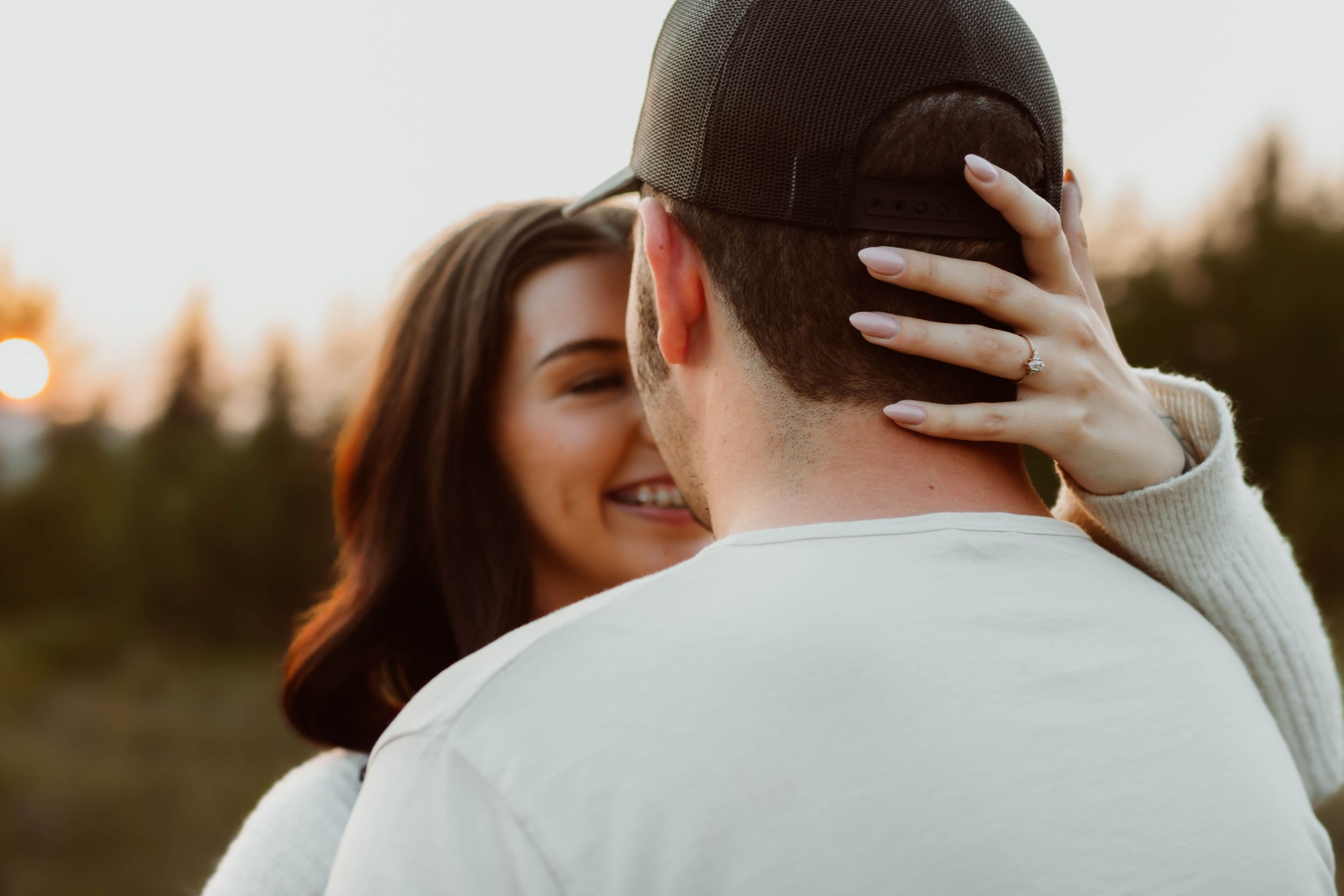 Intimate moment between couple embracing outdoors with woman's joyful expression visible.