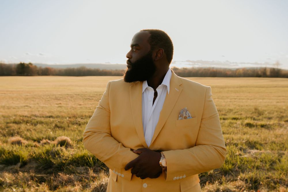 Person in a yellow suit jacket poses in a sunlit meadow during golden hour.