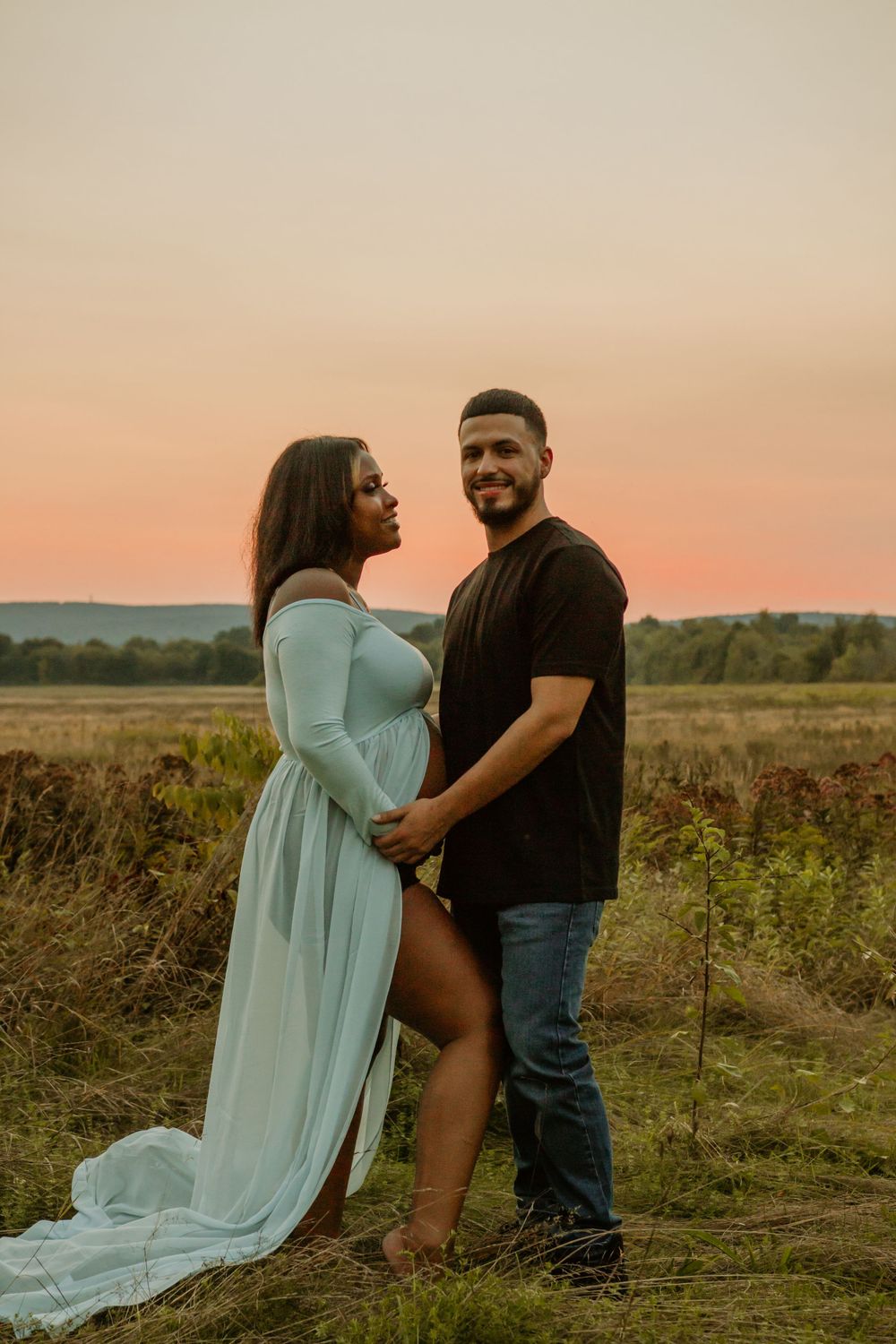 Romantic sunset photoshoot with couple in light blue dress and black shirt in an open field.