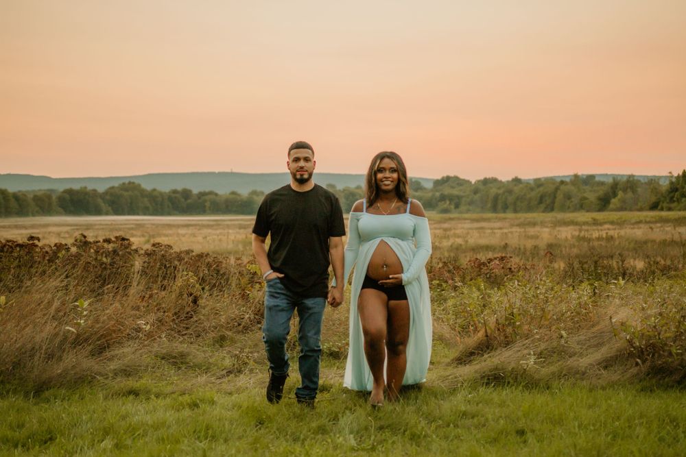 Maternity photo with couple posing in field during golden hour sunset.