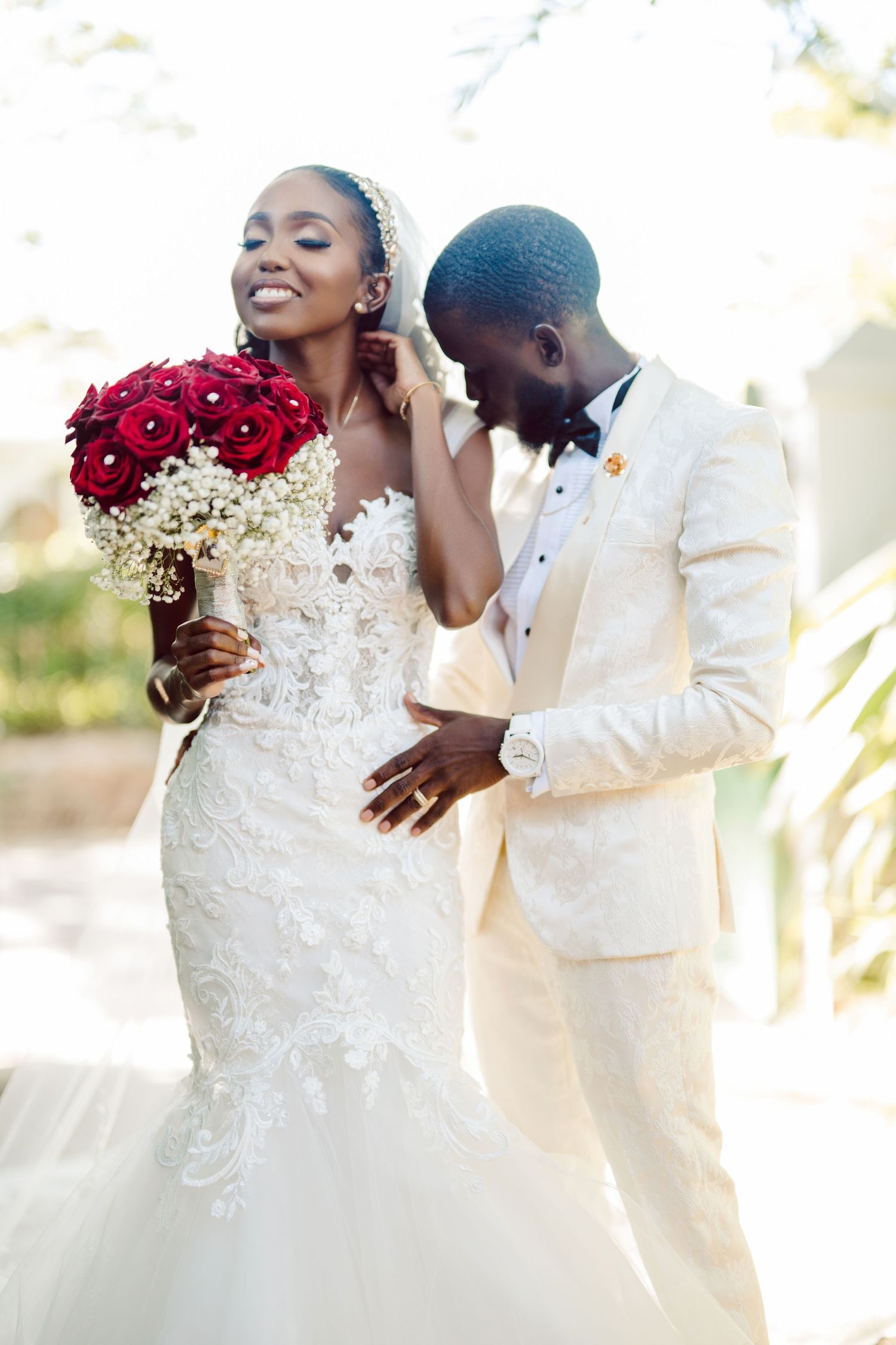 A joyful wedding couple embraces while holding a striking red and white bouquet.