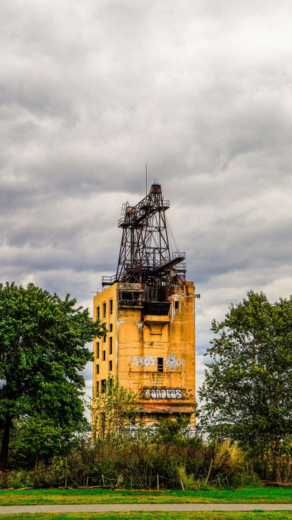 Abandoned yellow industrial tower with metal framework against stormy sky.