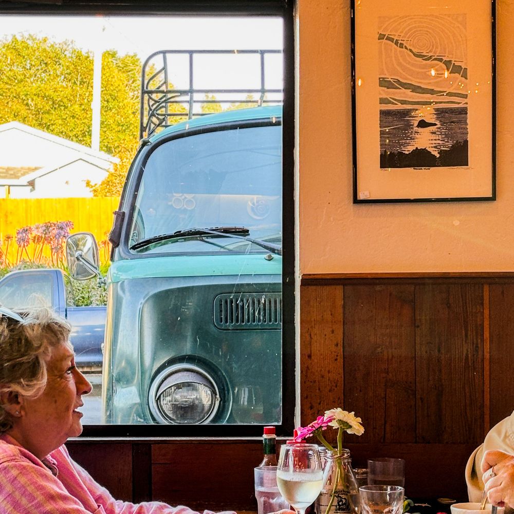 View through a diner window showing a vintage turquoise vehicle parked outside.