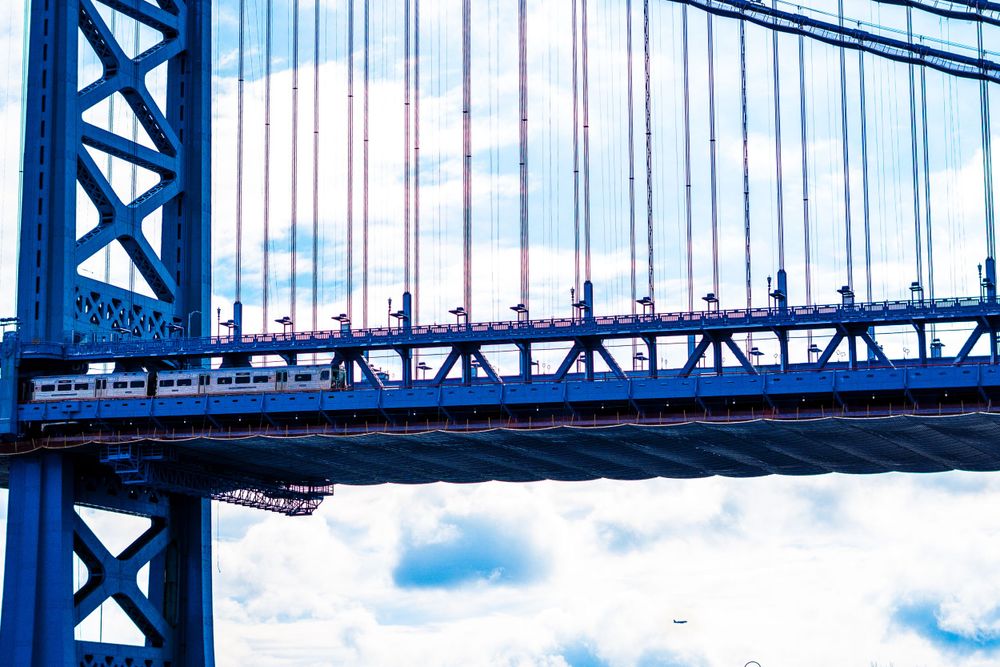 Low angle view of suspension bridge cables against blue sky with white clouds.