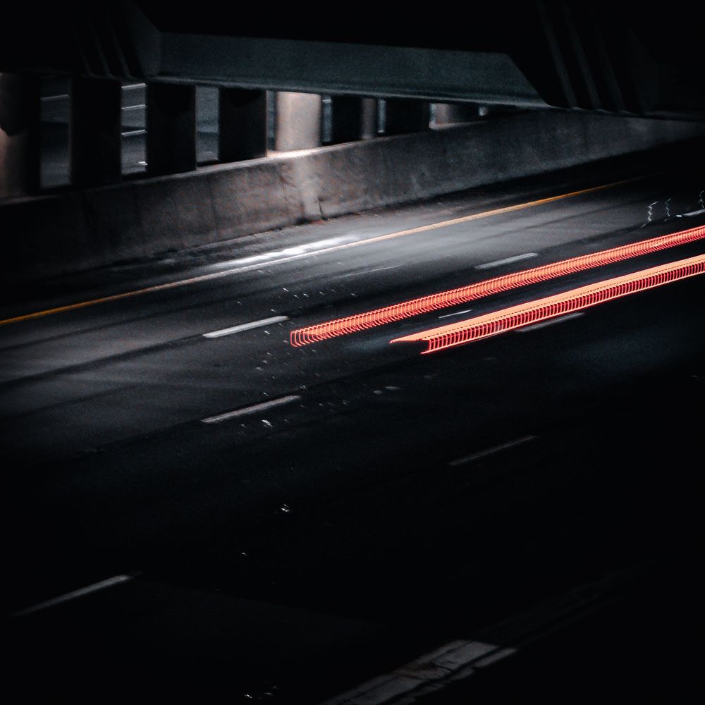 Long exposure shot of red light trails in a dark tunnel creating streaks of motion.