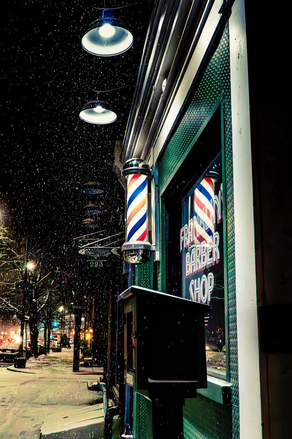 Traditional barber pole and shop exterior illuminated at night during snowfall.