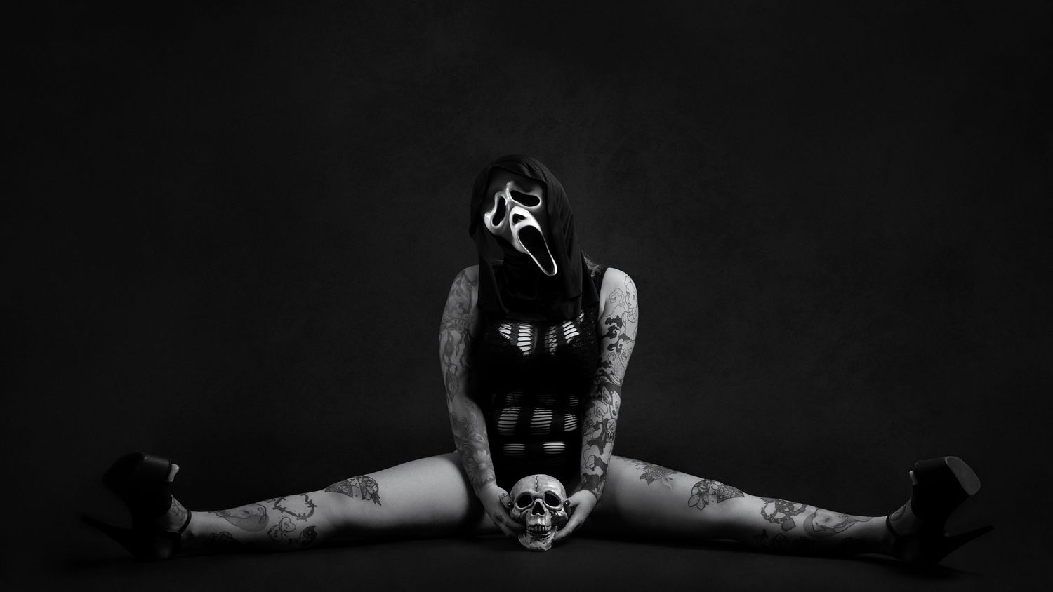 Artistic black and white photo of figure in dark clothing doing splits pose on floor.