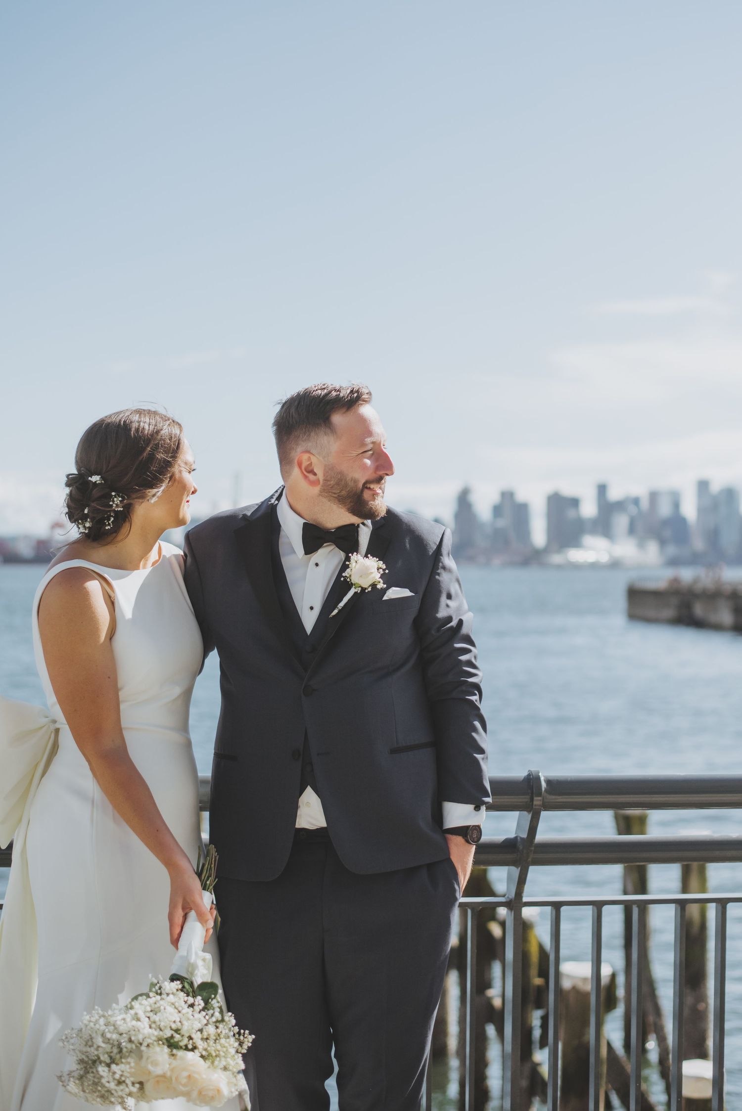 A couple shares a joyful moment on a waterfront pier with city skyline in the background.