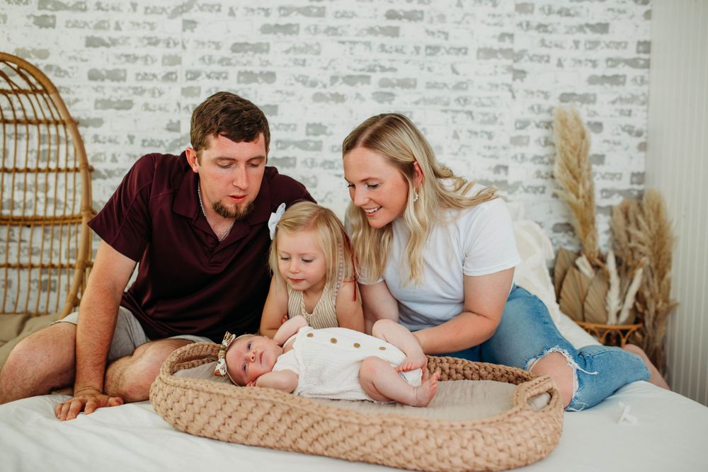 A tender family moment on a bed with a baby resting in a woven basket surrounded by cozy decor.
