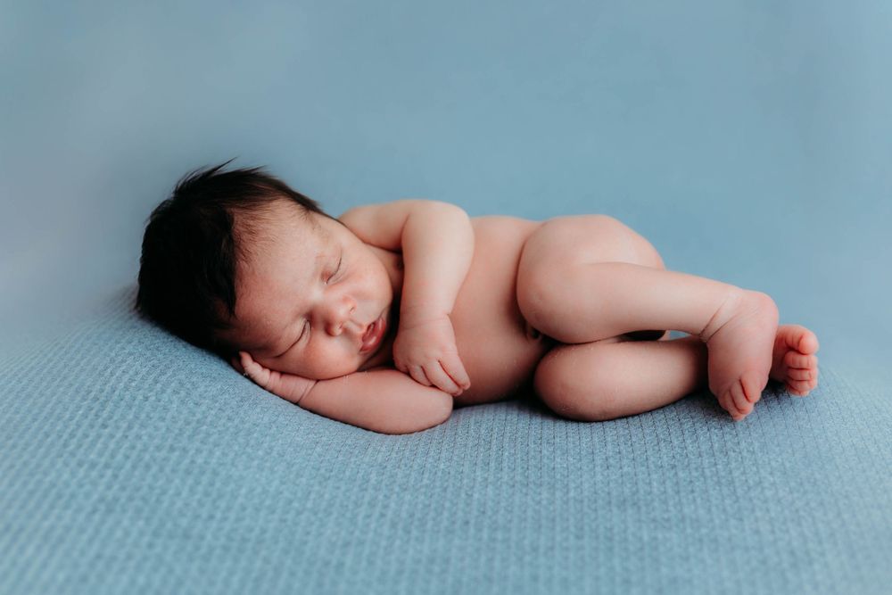 Peaceful newborn baby sleeps curled up on soft blue blanket during photo session.