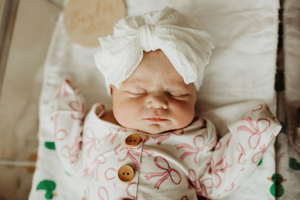 Sleeping infant wearing white bow headband and floral print outfit.