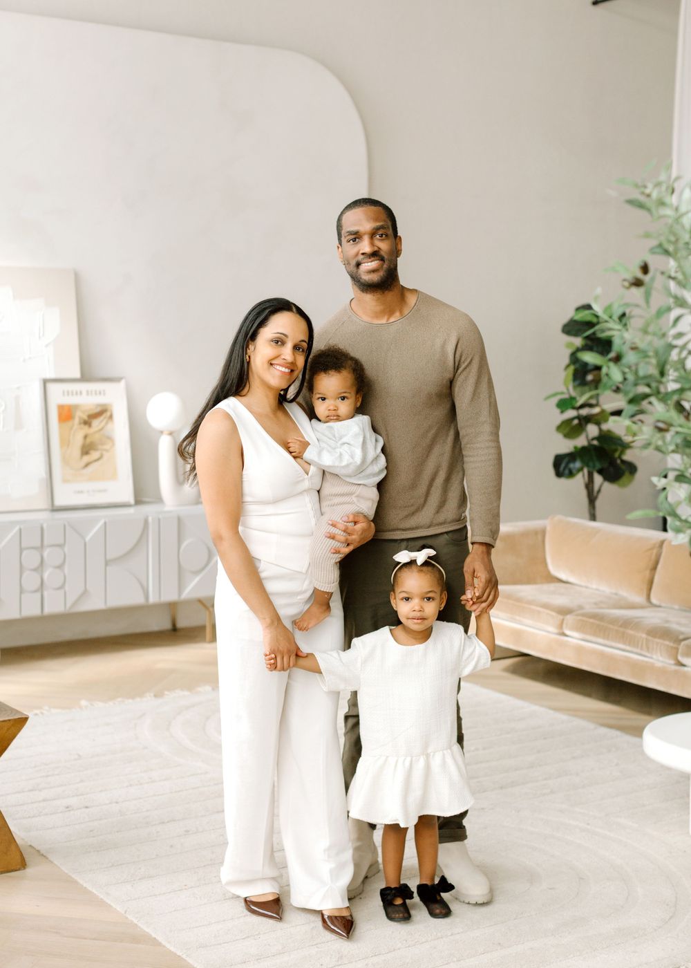 Family of four wearing coordinated white outfits pose together in modern living room.