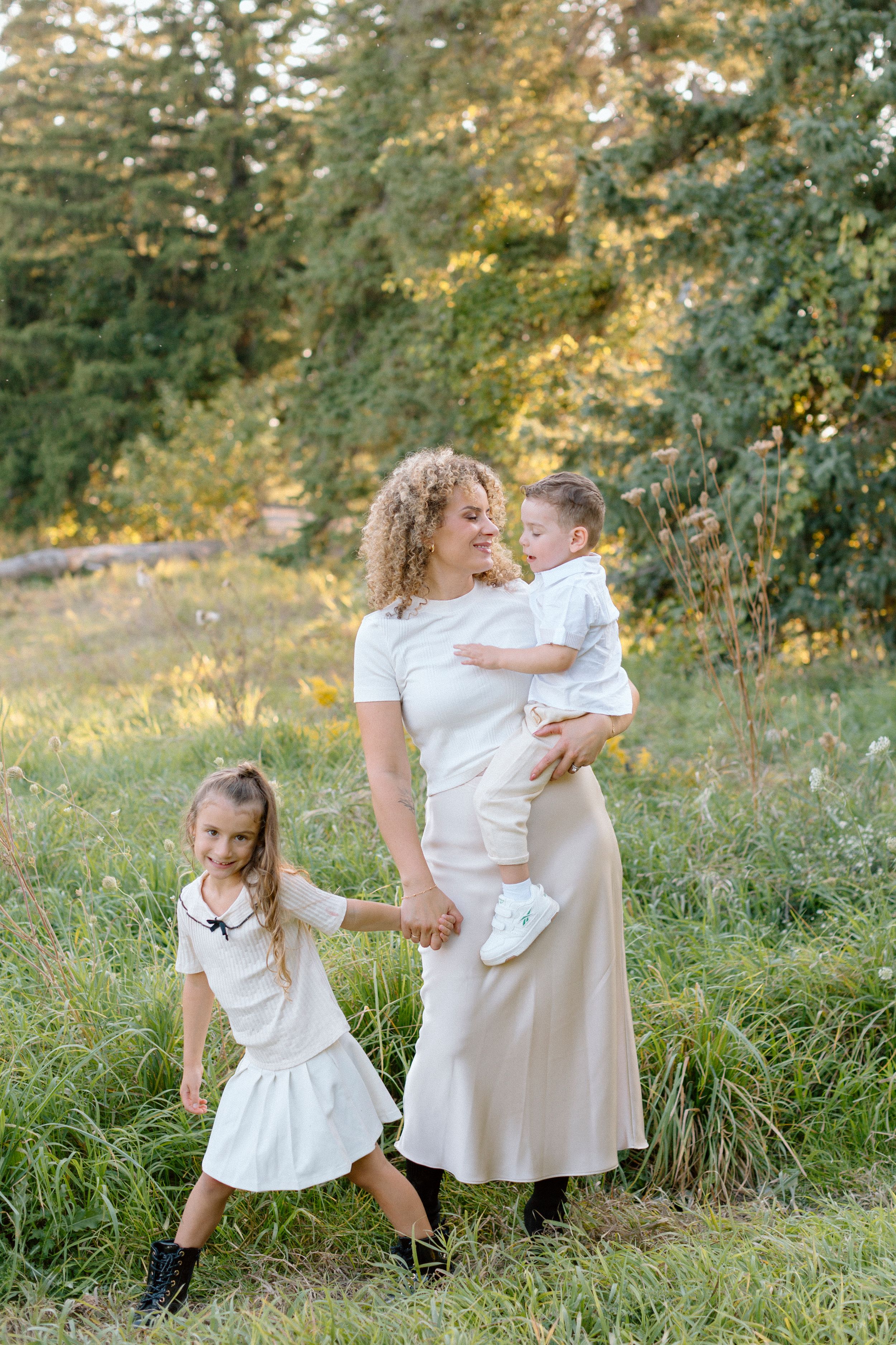 A family in white outfits enjoys a tender moment together in a sunlit meadow during golden hour.