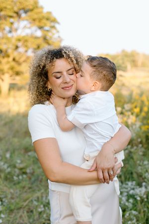 A tender embrace between parent and child wearing white clothing in a field of wildflowers at sunset.