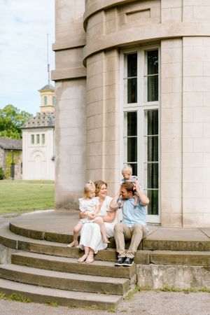 Family sitting together on stone steps of a historic building with tower in background.