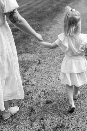 Black and white photo of parent and child holding hands while walking on gravel path.